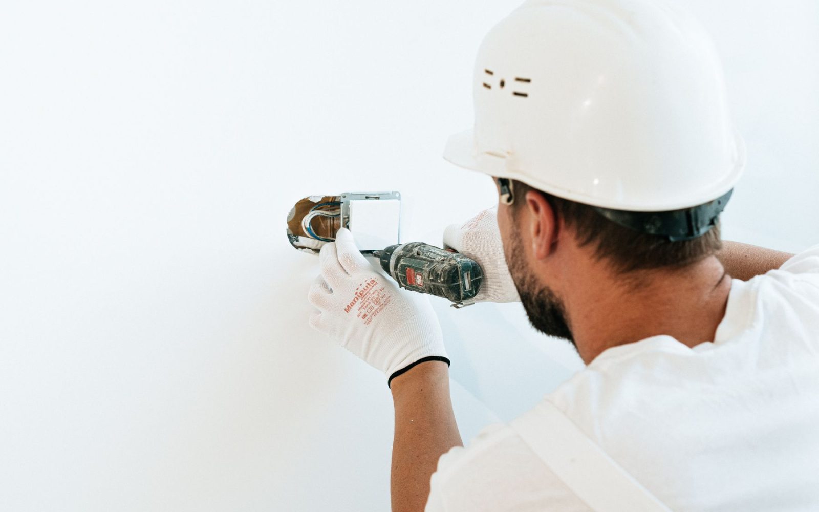 Elektriker mit Schutzhelm bohrt eine Unterputzdose in die Wand